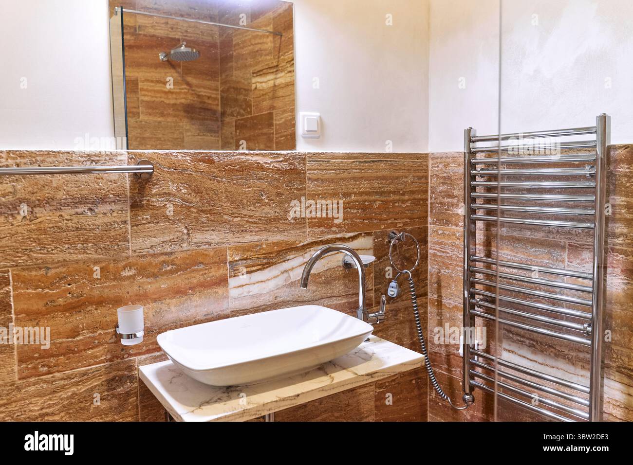 Ein modernes Bad mit eleganten Fliesenwänden, einem eleganten Waschbecken und Wasserhahn sowie einem Chrom-Handtuchhalter schaffen einen harmonischen und stilvollen Raum. Stockfoto