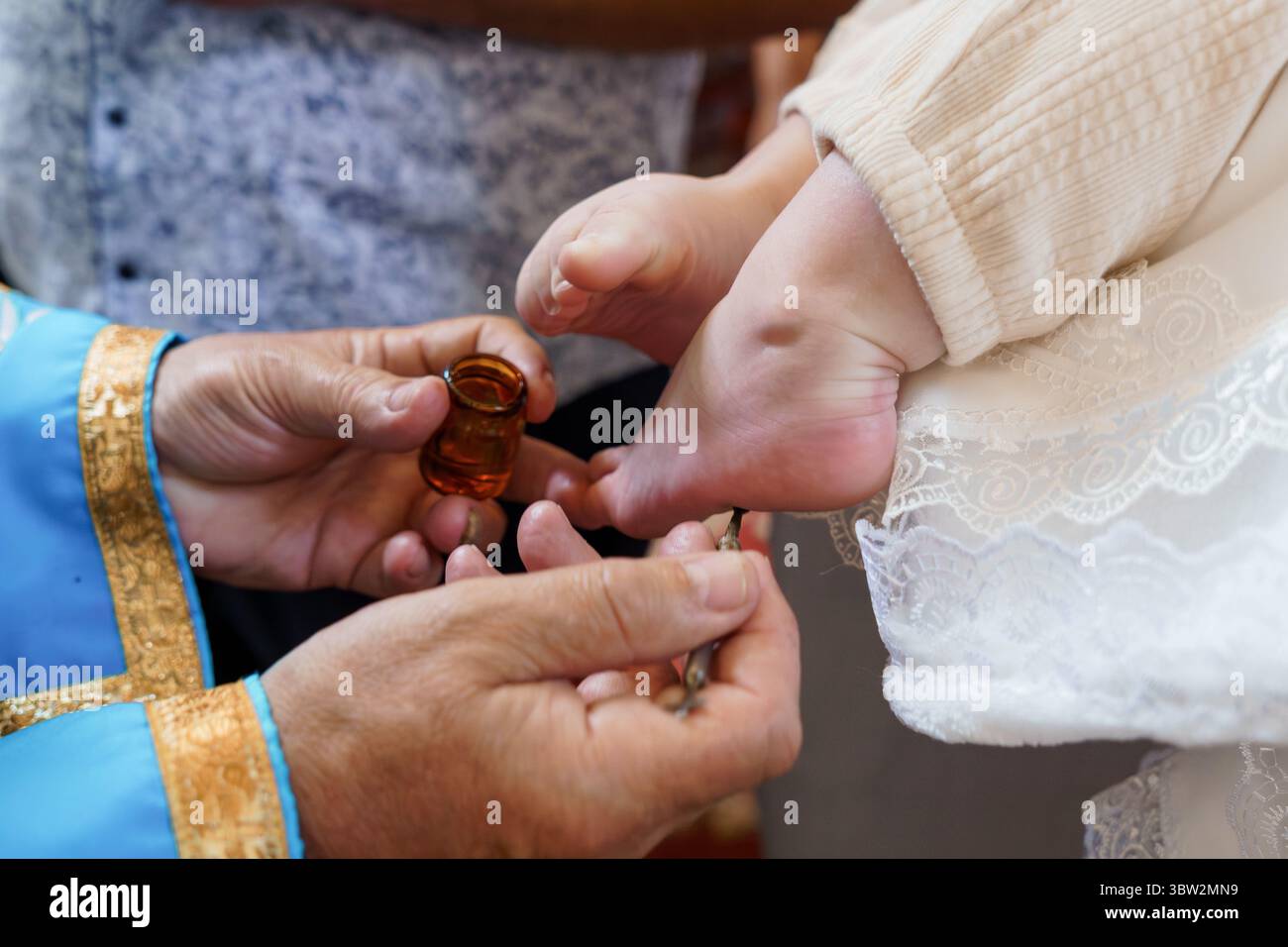 Nahaufnahme der Hände eines Priesters, die während einer christlichen Taufe den Fuß eines Babys mit heiligem Öl salben, was für Reinigung, Glauben und Neuanfänge steht Stockfoto