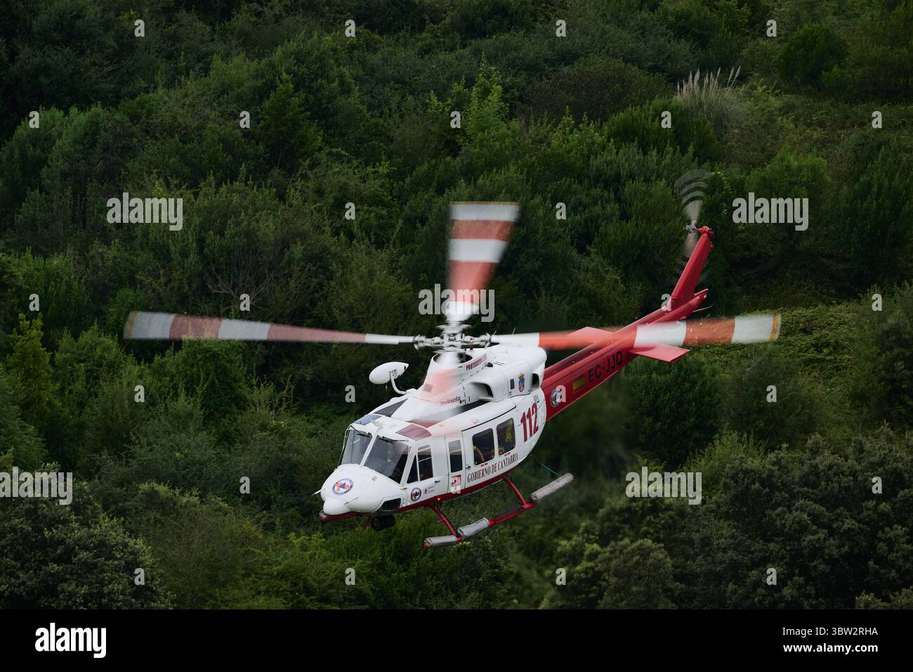 Rot-weißer Rettungshubschrauber, der über einen üppig grünen Wald fliegt und medizinische Notdienste sowie Such- und Rettungsoperationen bereitstellt Stockfoto