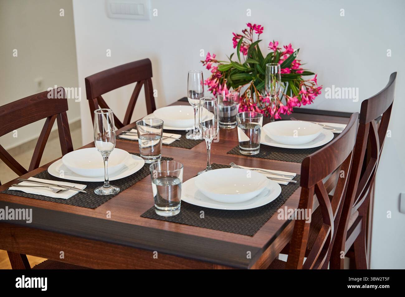 Ein moderner Esstisch mit Tellern, Gläsern und Besteck, elegant eingerichtet mit einem floralen Herzstück, bietet eine ruhige und stilvolle Einrichtung Stockfoto