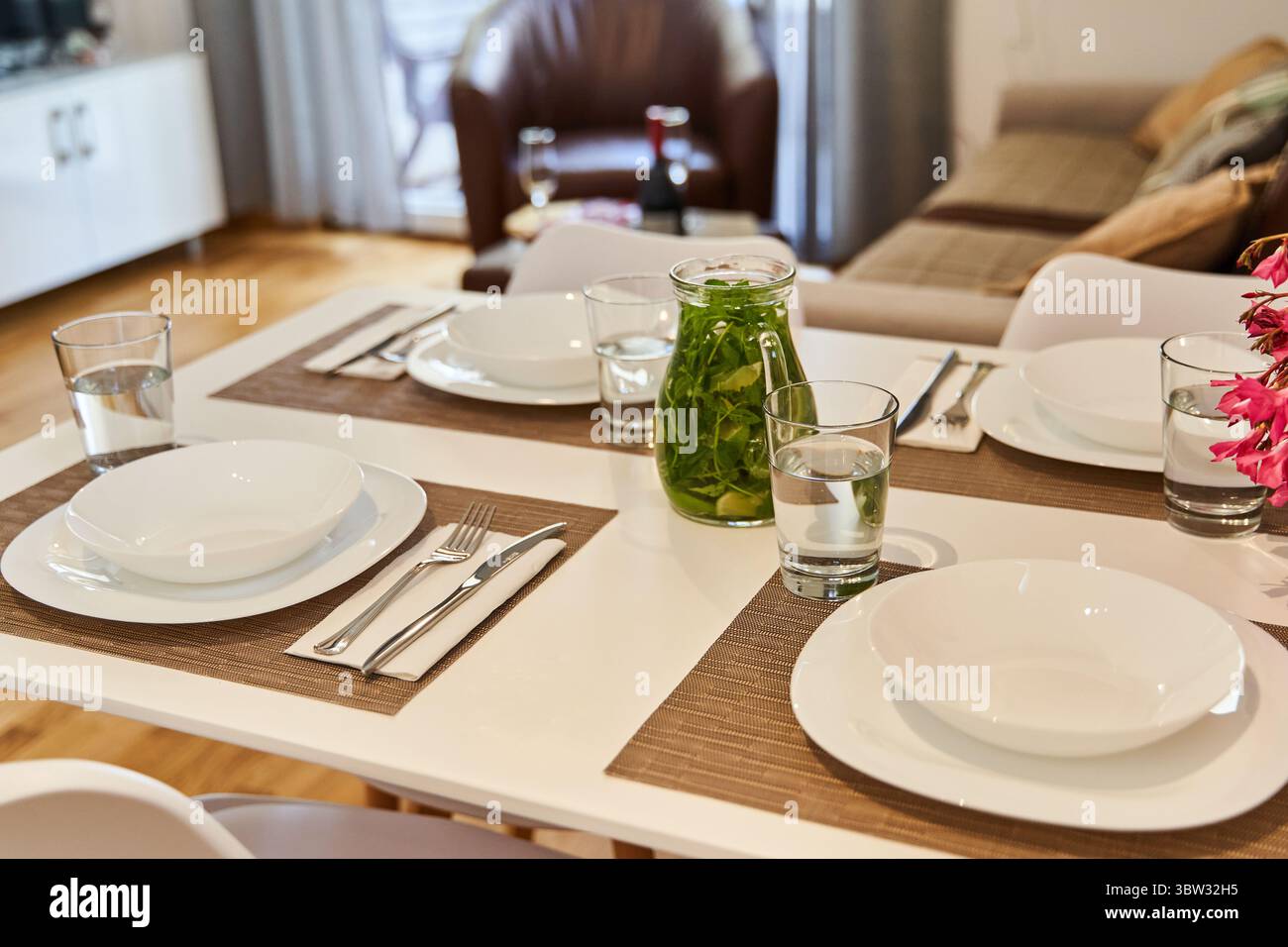Ein ordentlich angeordneter Esstisch mit weißen Tellern, Besteck, Glasgläsern und Gläsern in einem modernen und einladenden Wohnzimmer. Stockfoto