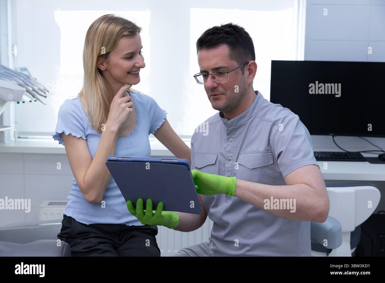 Patienteninteraktion in einer modernen Zahnklinik: Ein Zahnarzt berät eine weibliche Patientin mit einem Tablet in einer komfortablen und einladenden Umgebung Stockfoto