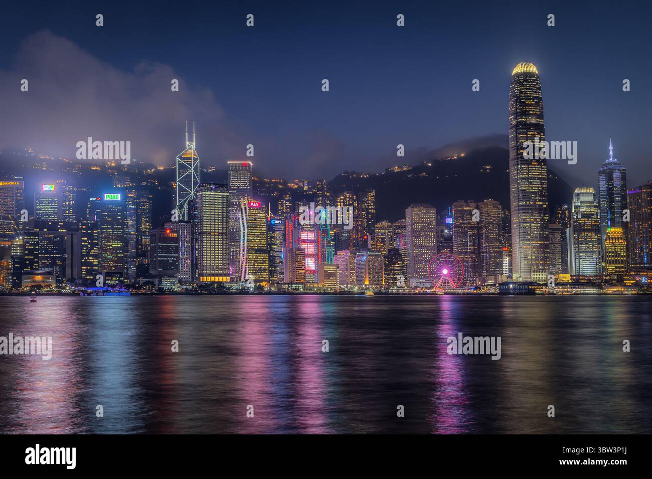 Hongkong, Hongkong - 14. Juli 2025: Blick auf die Skyline der Stadt, die mit leuchtenden Lichtern im ruhigen Hafenwasser gespiegelt wird, eine Symphonie aus urbaner Energie und ruhiger Reflexion. Stockfoto