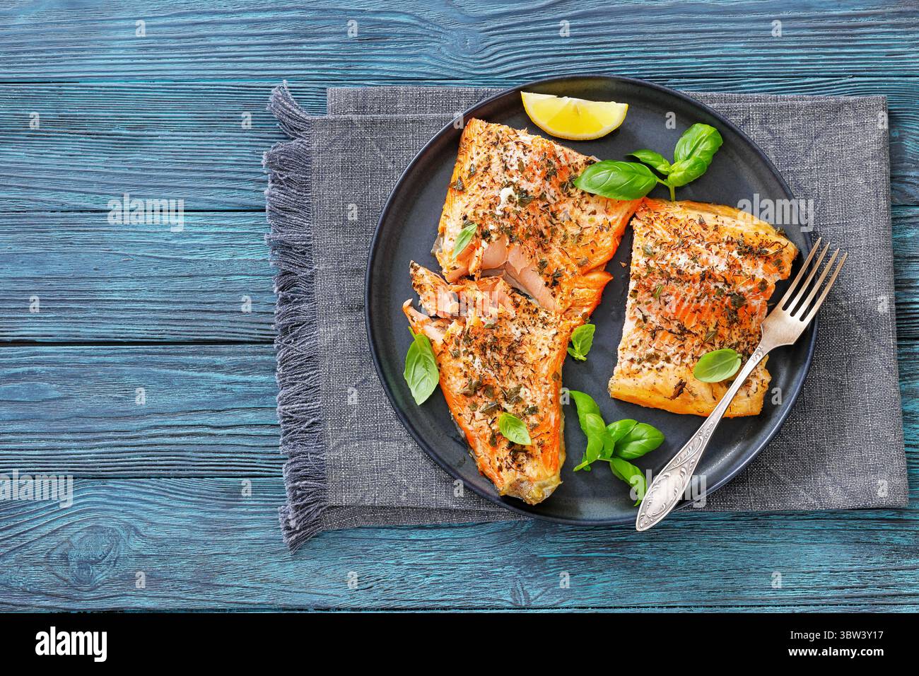 Gegrillte ganze Lachsfilets mit Haut auf einem Teller mit frischem Basilikum, Zitronenscheiben, Gabel auf Holztisch, Draufsicht, freier Platz, flach liegend, Nahaufnahme, nicht Stockfoto