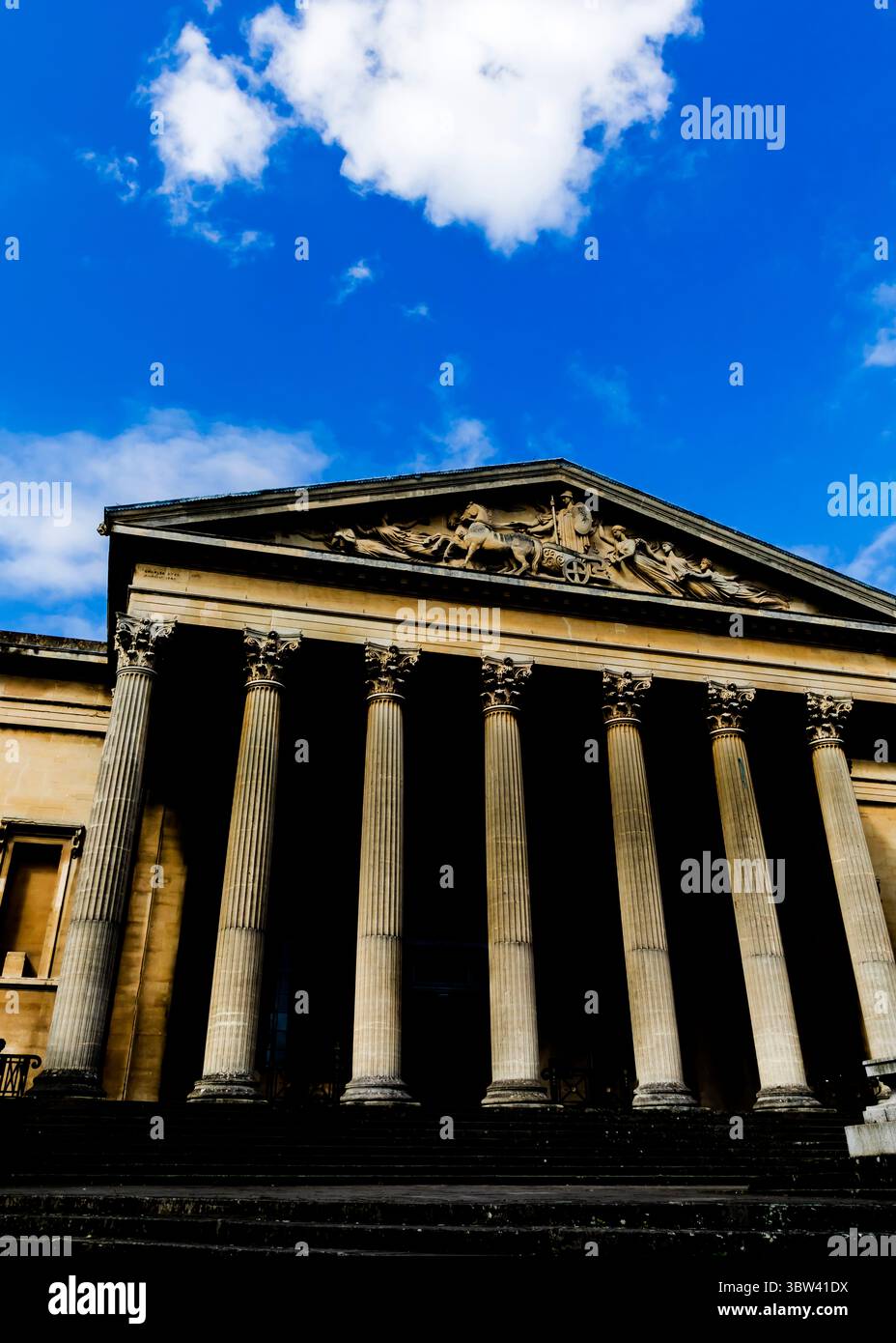 Eine Niedrigwinkelaufnahme eines Gebäudes mit großen Säulen und einem detaillierten Fries unter einem blauen Himmel mit Wolken. Stockfoto