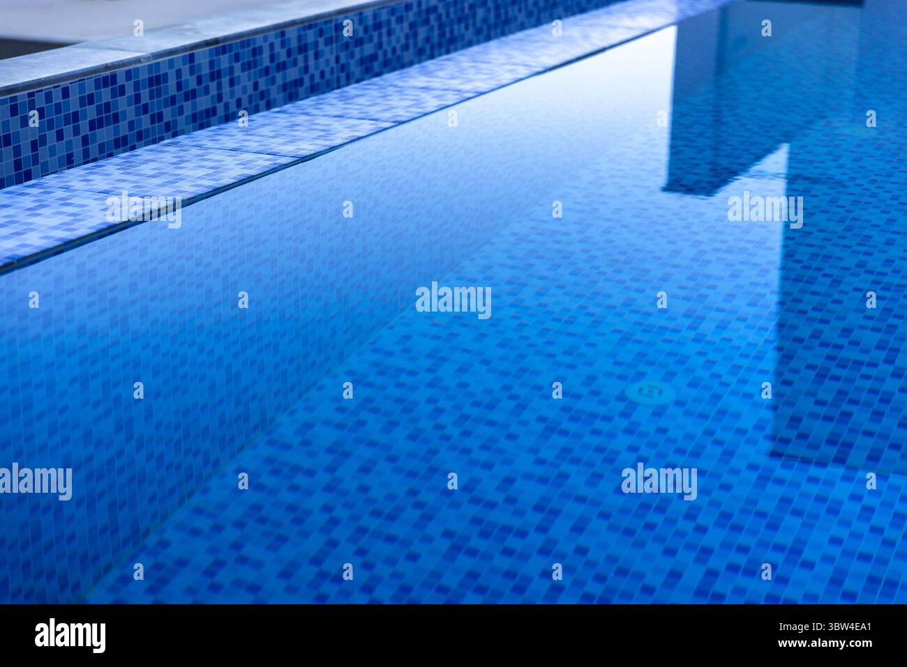 Blau gefliester Swimmingpool mit klarem reflektierendem Wasser, minimalistischem Design und ruhiger Atmosphäre, perfekt zum Entspannen oder eleganten Architekten Stockfoto