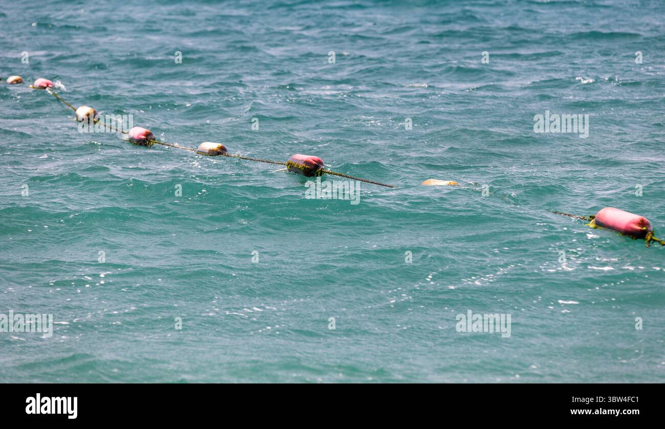 Bojen schweben auf einer Linie, die die ruhige Meeresoberfläche trennt und die Seeschifffahrt und -Sicherheit repräsentieren. Stockfoto
