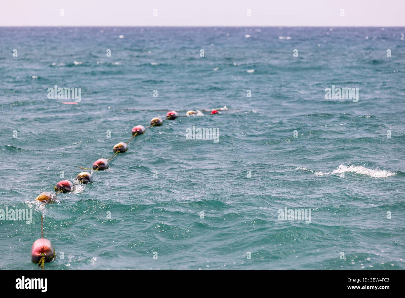 Rote Kunststoffbojen schweben auf einer Linie, die die ruhige Meeresoberfläche trennt und die Seeschifffahrt und -Sicherheit repräsentieren Stockfoto