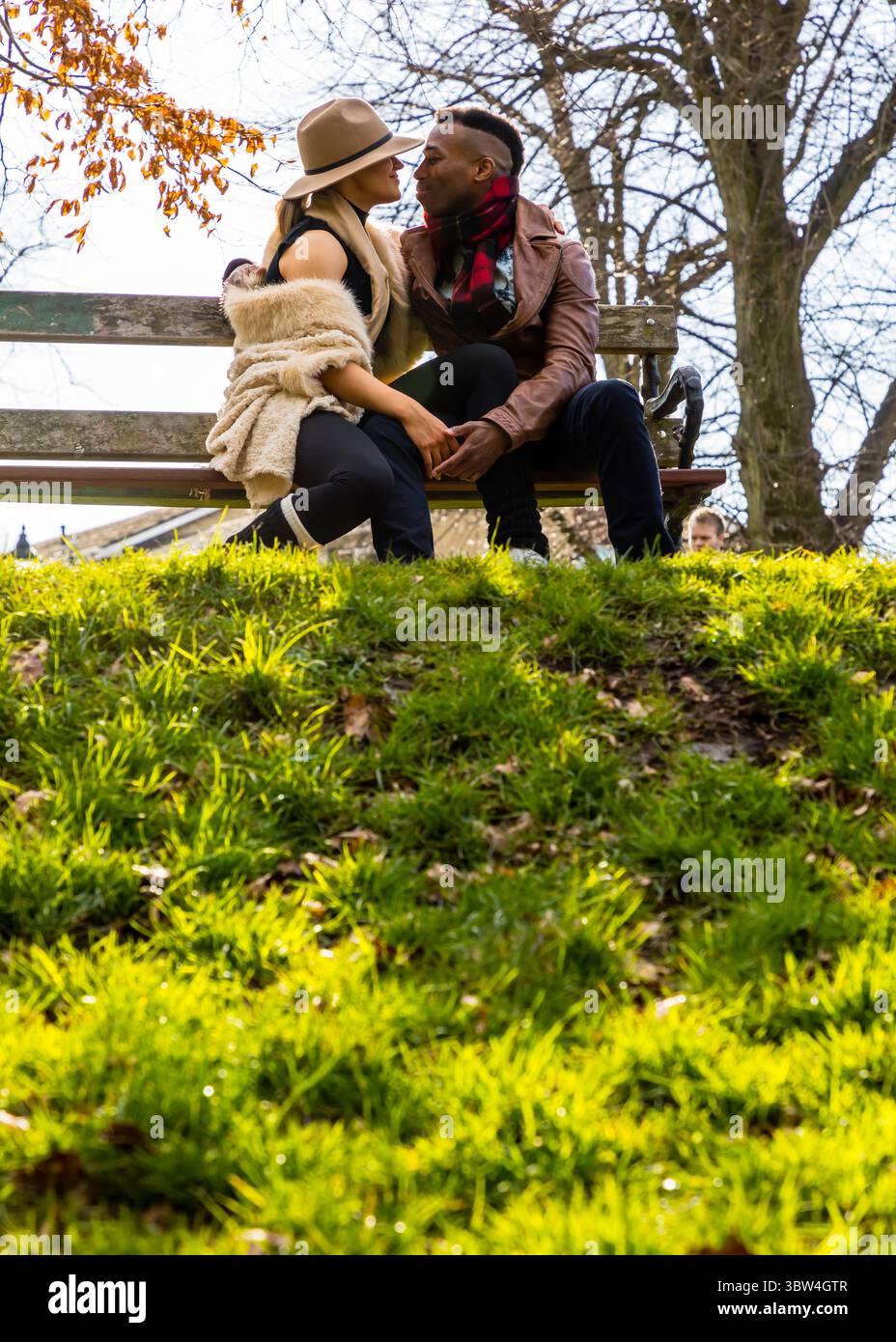 Ein Paar sitzt auf einer Bank im Park, hält die Hände und sieht sich an. Die Frau trägt einen Hut und einen Pelzschal, während der Mann trägt Stockfoto