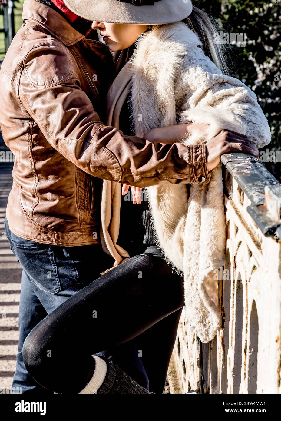 Ein Paar umarmt sich auf einer Brücke, der Mann in einer Lederjacke und die Frau in einem Pelzmantel und Hut. Stockfoto