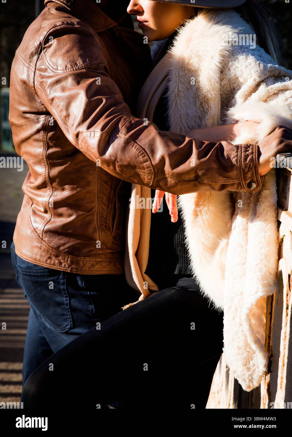 Ein Paar umschließt sich, mit dem Mann in einer braunen Lederjacke und der Frau in einem weißen Pelzmantel. Stockfoto