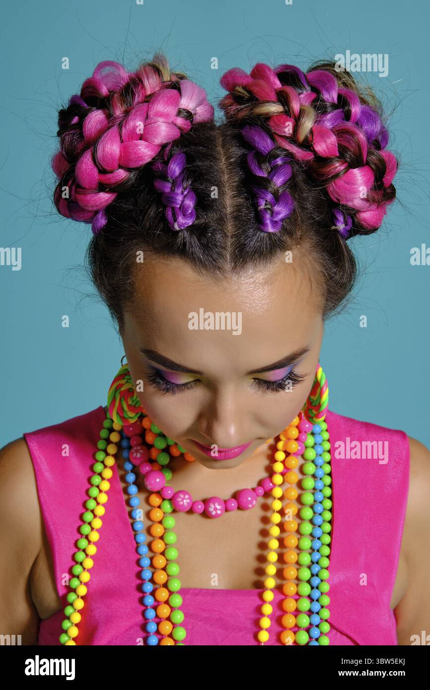 Nahaufnahme einer lustige Frau mit einem bunten Zöpfe Frisur und Make-up, im Studio vor einem blauen Hintergrund posiert und blickte nach unten. Stockfoto
