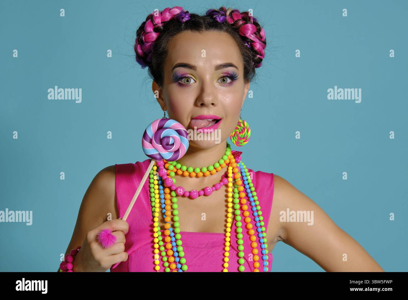 Nahaufnahme einer attraktiven Dame mit einem bunten Zöpfe Frisur und Make-up, im Studio vor einem blauen Hintergrund posiert, lecken a l Stockfoto