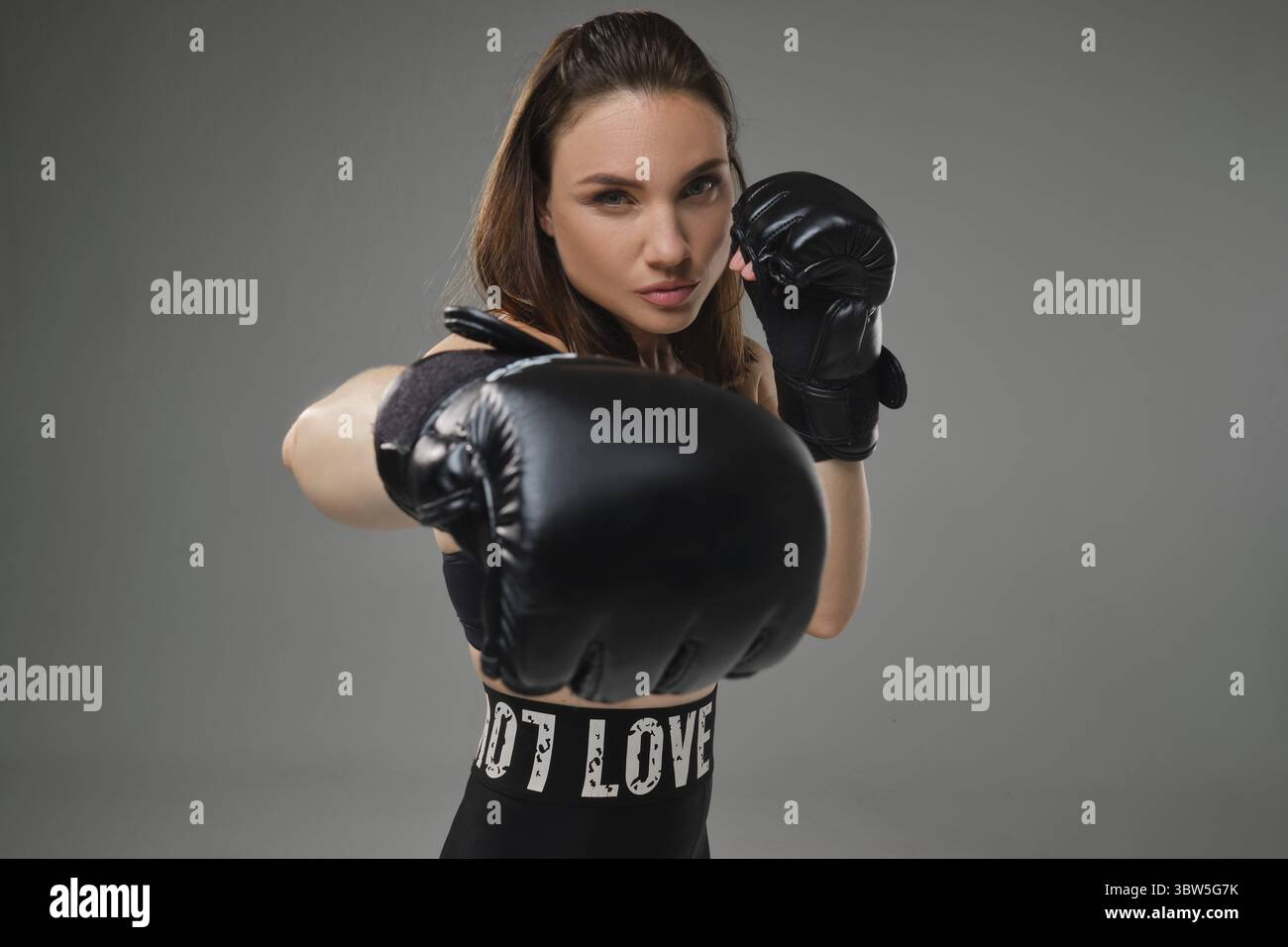 Nahaufnahme einer jungen, attraktiven Jungfrau mit lockeren Haaren, gekleidet in einem Sporttop, Leggings und Boxhandschuhen, sieht ihre Gegnerin während des Trainings an Stockfoto