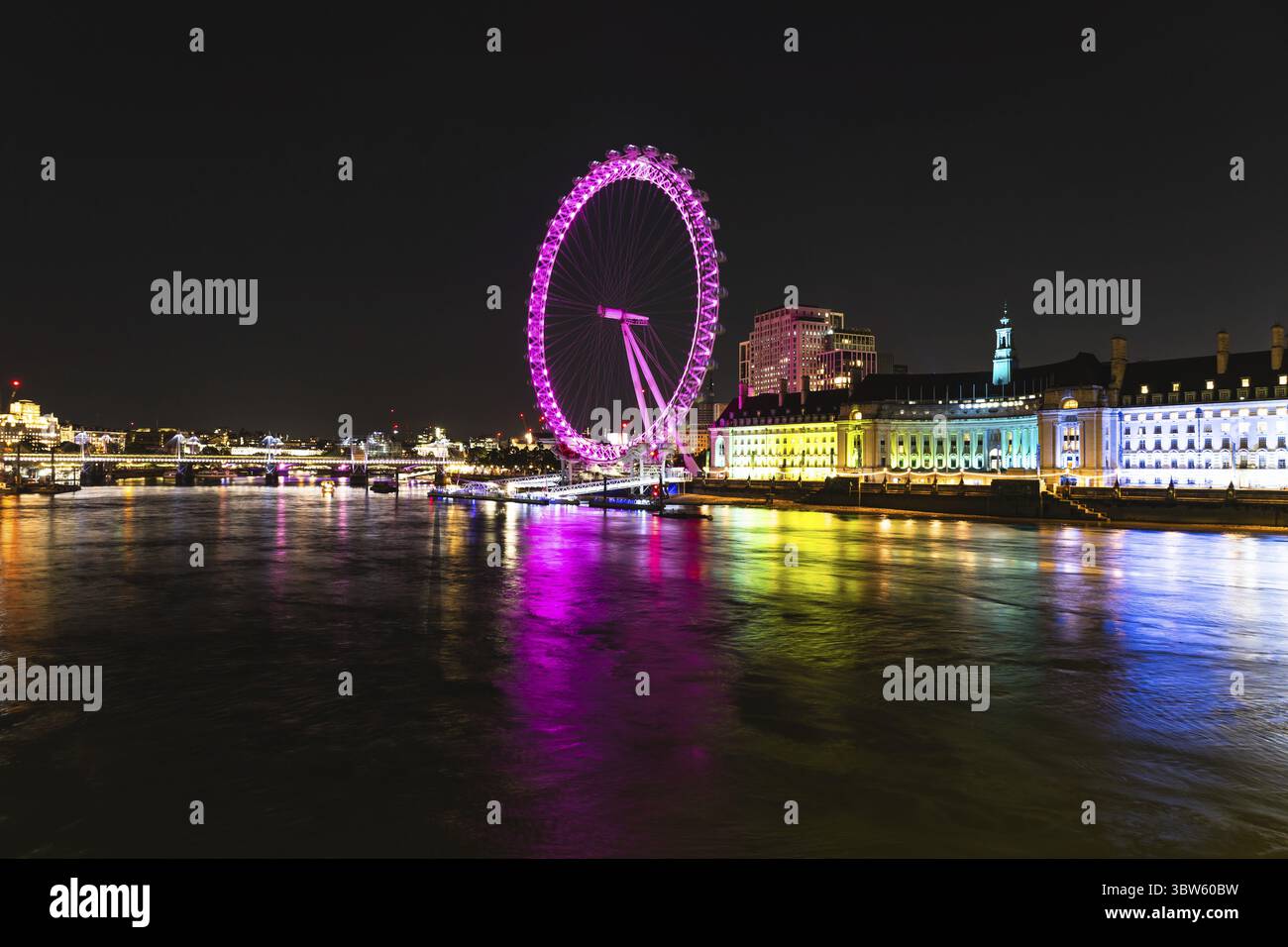 Ein atemberaubender Blick auf das London Eye, das nachts in leuchtenden Farben leuchtet, ergänzt durch ruhige Reflexionen der Themse Stockfoto