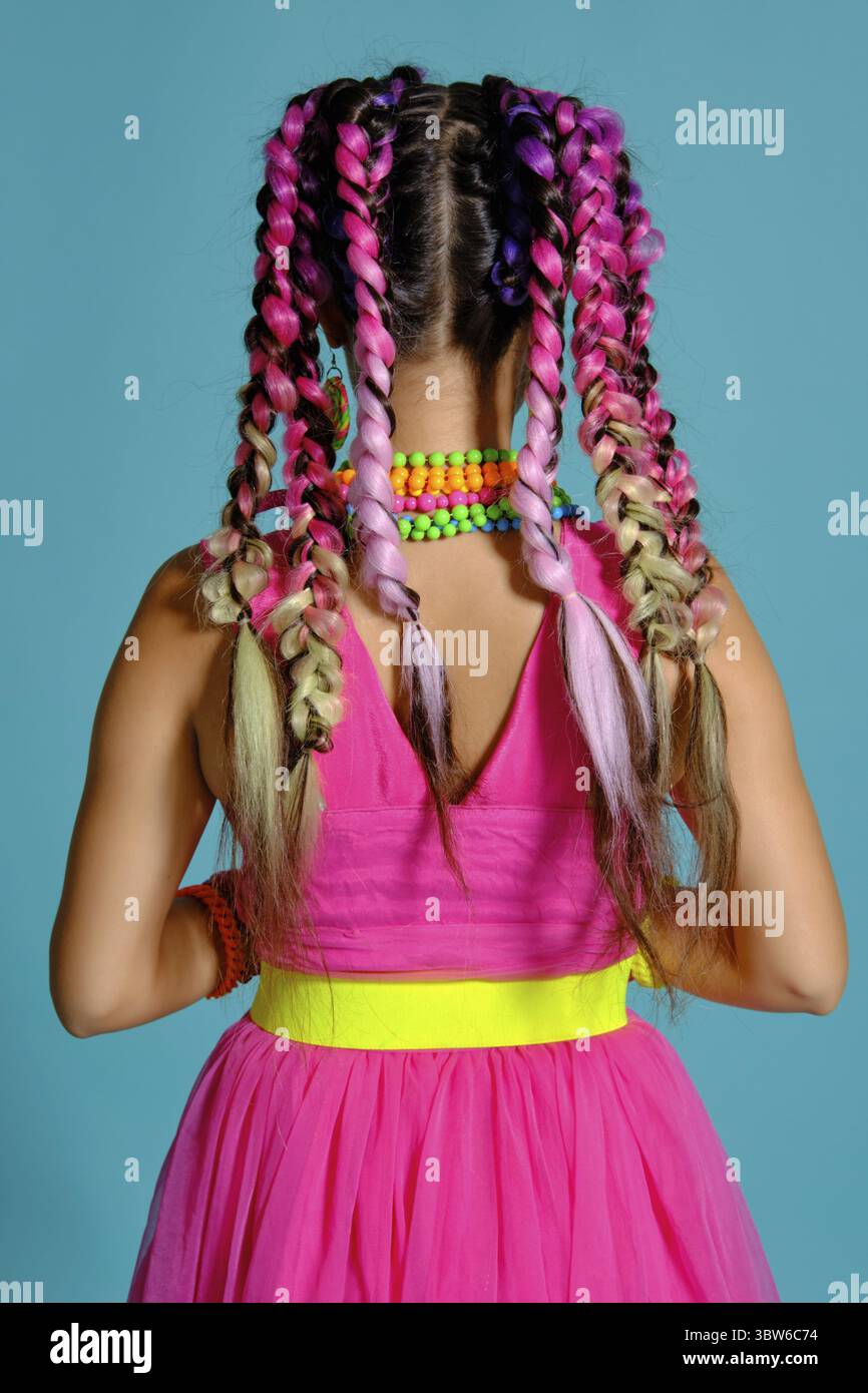 Nahaufnahme einer fröhliche Dame mit einem bunten Zöpfe Frisur und Make-up, posing Rücken an die Kamera im Studio vor einem blauen b Stockfoto