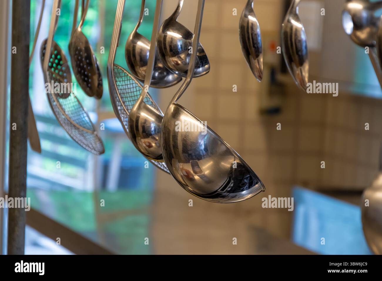 Ein Satz von Küchenlöffeln und Löffeln aus Metall hängt an einer Schiene in einer professionellen Küche Stockfoto