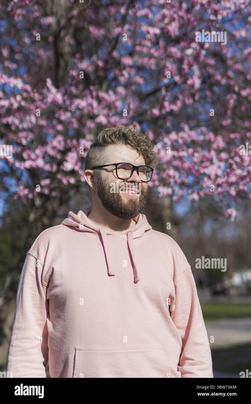 Mann-Allergie genießt nach Behandlung von Saisonallergie im Frühjahr. Porträt eines glücklichen bärtigen Mannes, der im Frühling vor einem Blütenbaum lächelt. S Stockfoto