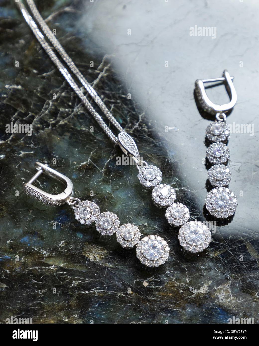 Das hübsche Set aus Diamant-Halskette und Ohrringen liegt auf einer dunkelgrünen und blau marmorierten Oberfläche Stockfoto
