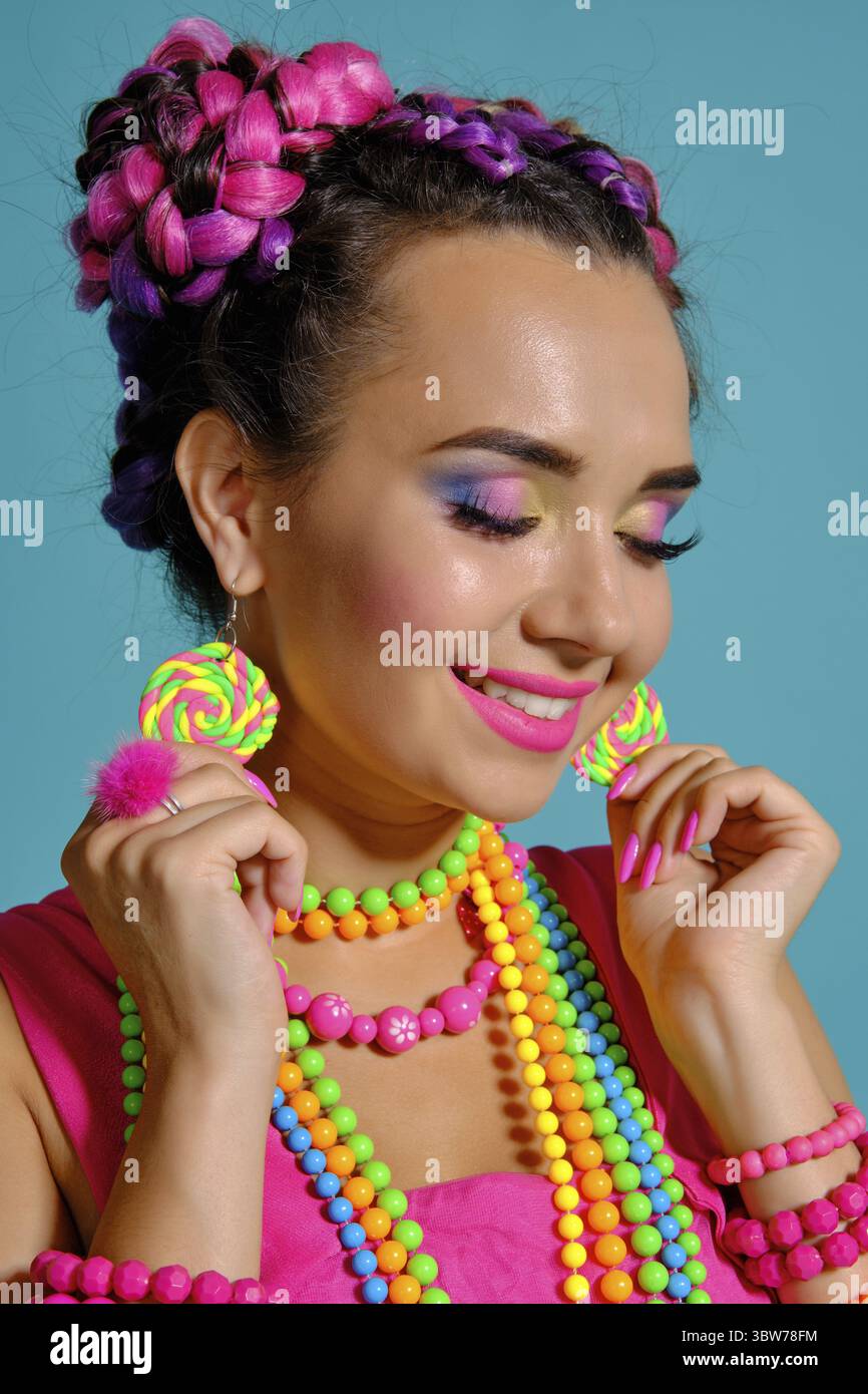 Nahaufnahme einer Funny Girl mit einem bunten Zöpfe Frisur und Make-up, im Studio vor einem blauen Hintergrund posiert, lächelnd mit Clos Stockfoto