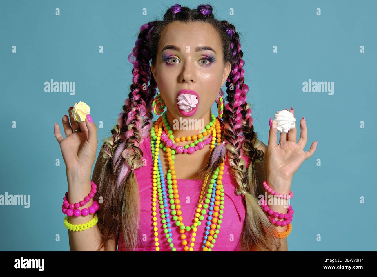 Nahaufnahme einer faszinierende Dame mit einem bunten Zöpfe Frisur und Make-up, im Studio vor einem blauen Hintergrund posiert, Mar Stockfoto