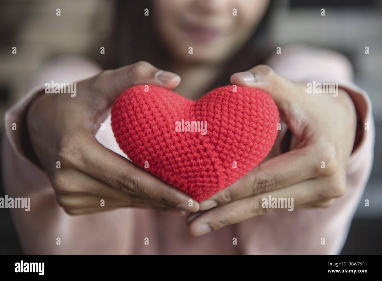 Großes rotes Garn, das Herz hält und mit der Frauenhand nach vorne gibt. Liebe und Zuneigung im Valentinstag-Konzept. Romantisches Objekt und Gesundheitsfürsorge Stockfoto