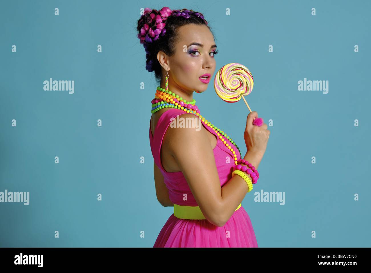 Nahaufnahme von einem attraktiven Mädchen mit einem bunten Zöpfe Frisur und Make-up, posing seitwärts stehend im Studio vor einem blauen Hinterg Stockfoto