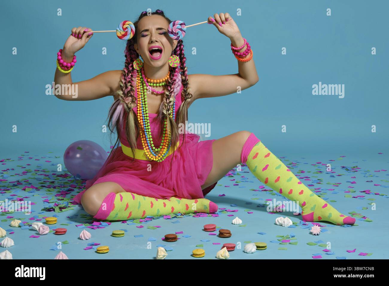 Volle Länge Foto von einem erfreulichen Maiden mit einem bunten Zöpfe Frisur und Make-up. Posiert im Studio mit Luftballons, Macarons, marshma Stockfoto