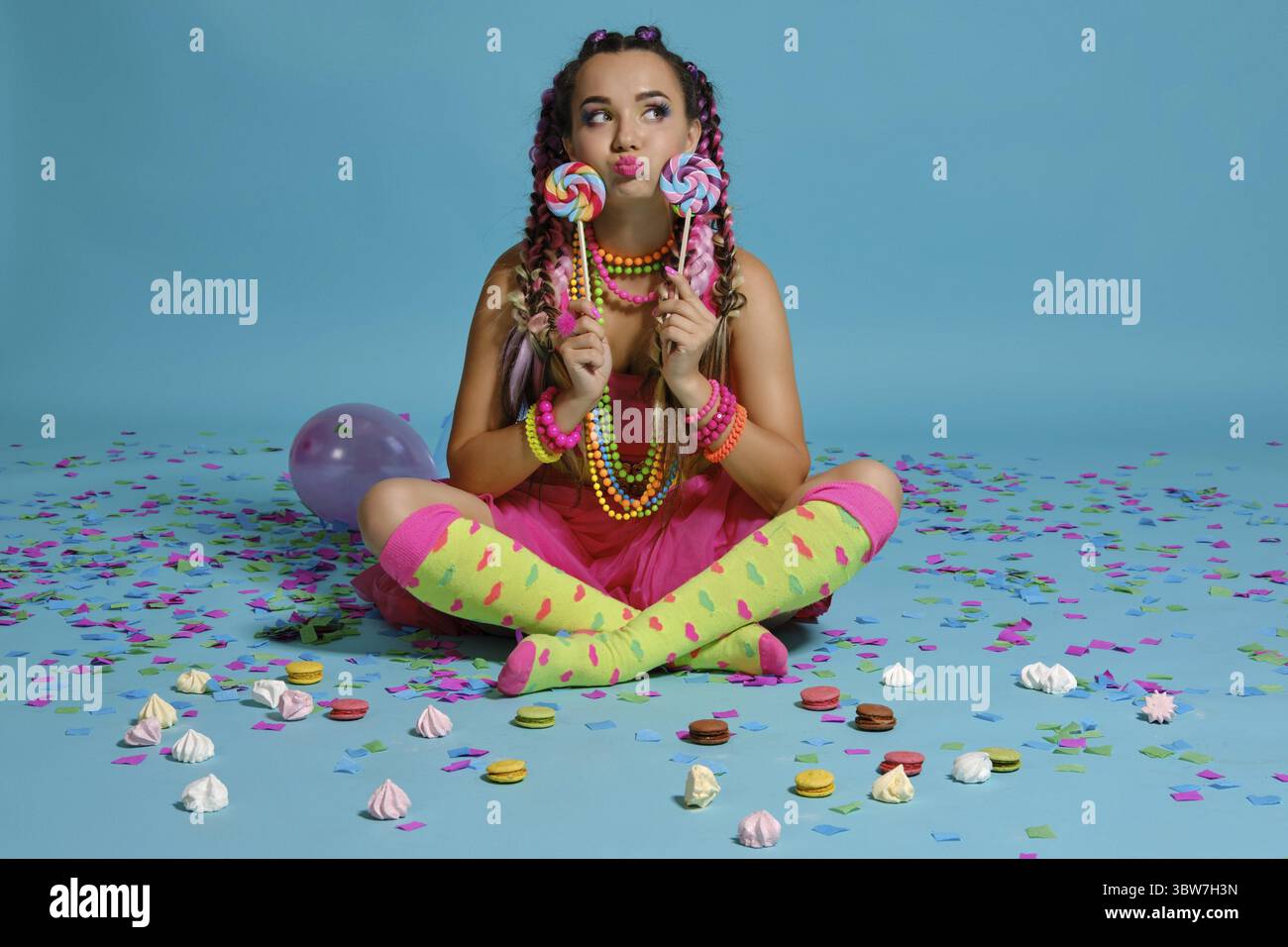 Volle Länge Foto einer schönen Frau mit einem bunten Zöpfe Frisur und Make-up. Posiert im Studio mit Luftballons, Macarons, marshmall Stockfoto