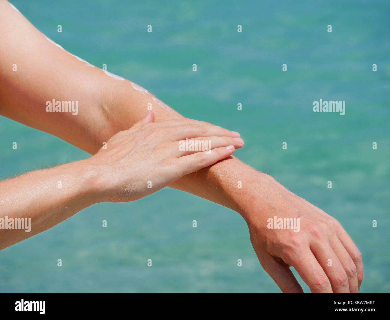 Ein Mann am Strand trägt Sonnencreme auf seine Hände vor dem Hintergrund des Meerwassers. Hautpflege, Sonnenschutz und Strandurlaubskonzept. Stockfoto