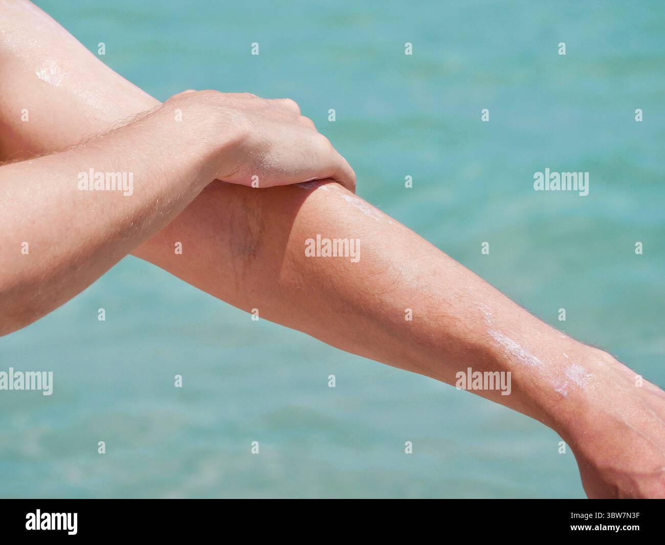 Ein Mann am Strand trägt Sonnencreme auf seine Hände vor dem Hintergrund des Meerwassers. Hautpflege, Sonnenschutz und Strandurlaubskonzept. Stockfoto