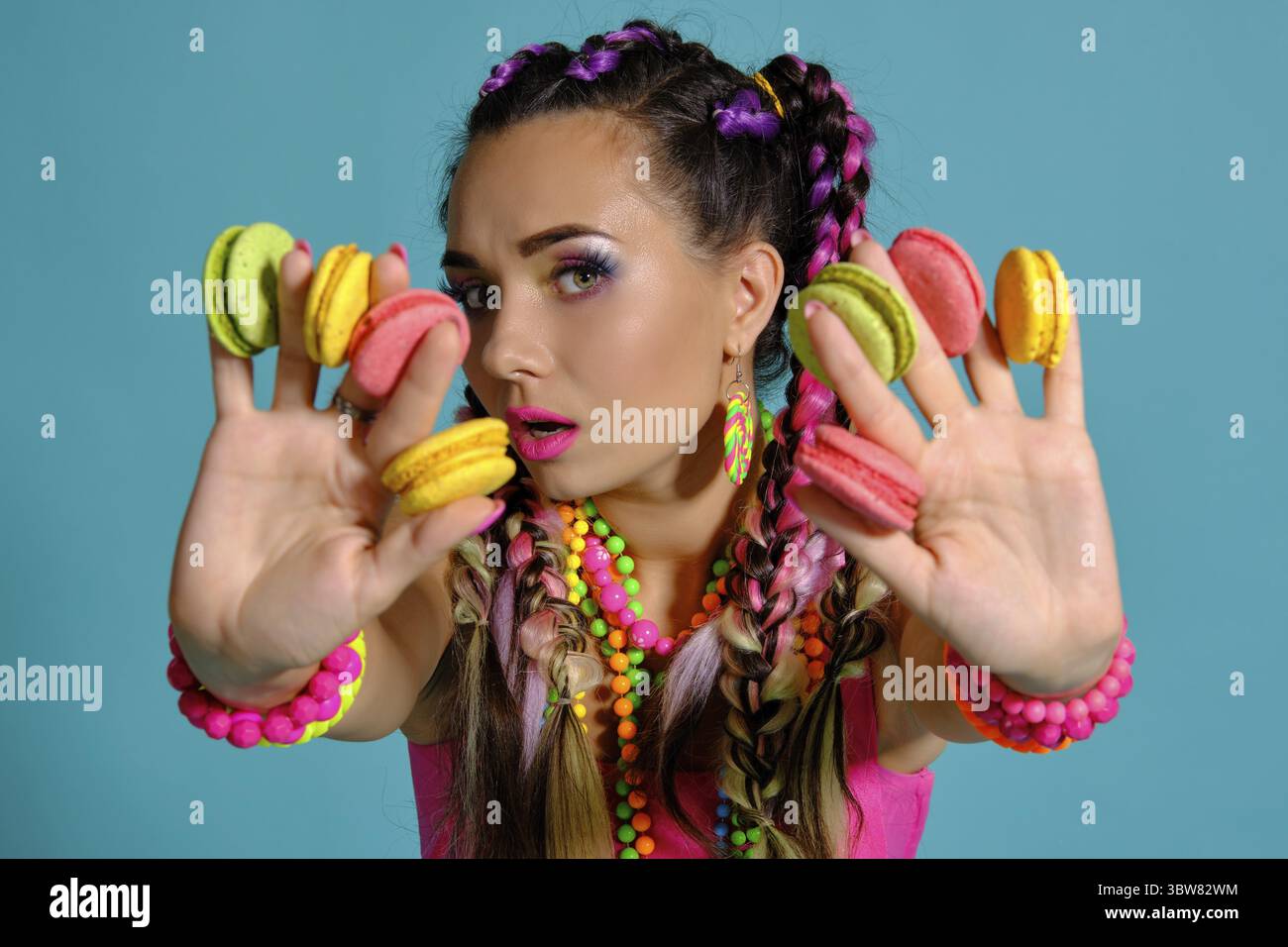 Nahaufnahme einer schönen Frau mit einem bunten Zöpfe Frisur und Make-up, im Studio vor einem blauen Hintergrund posiert, Ma Stockfoto