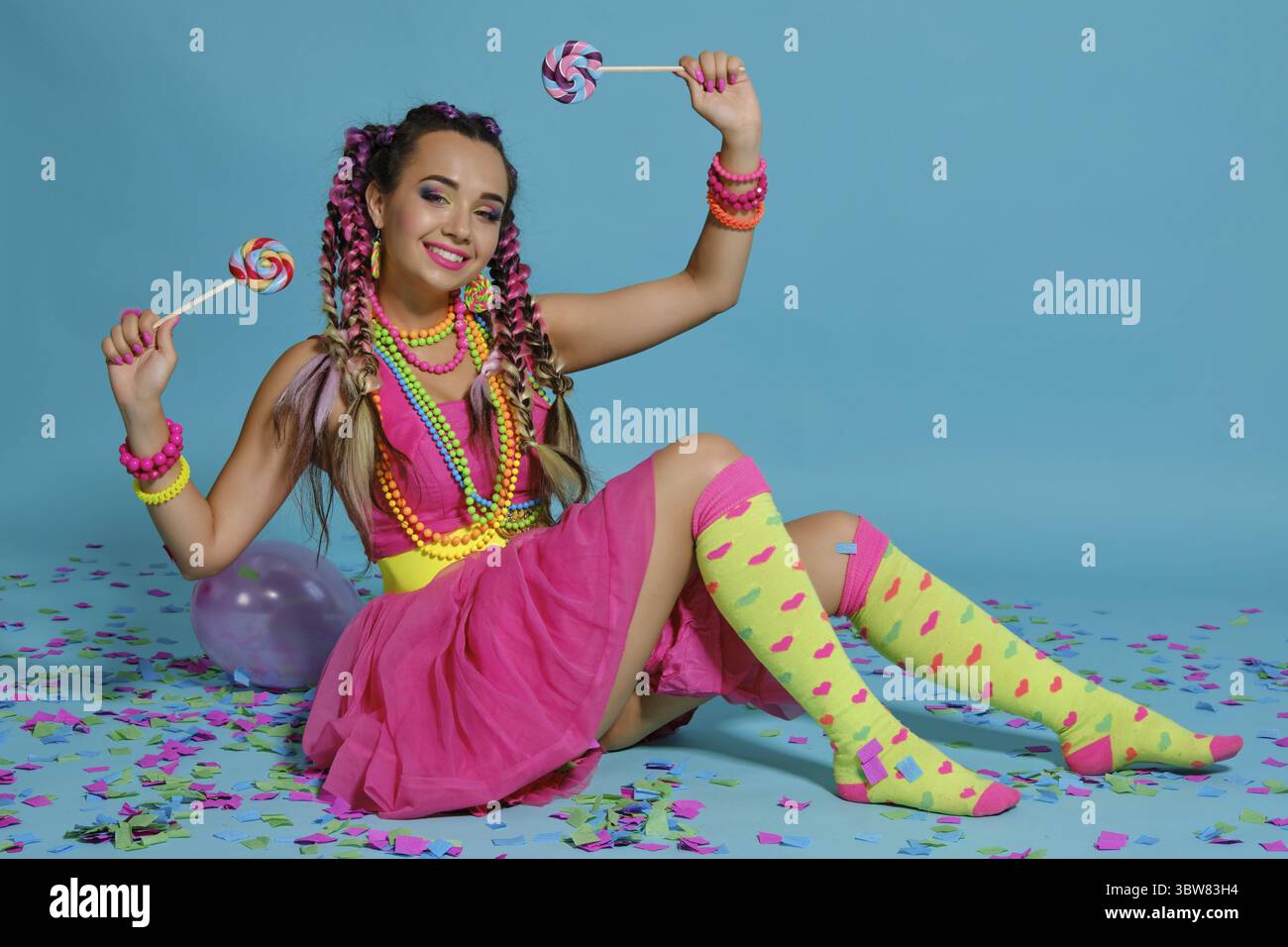 Volle Länge Foto von einem erfreulichen Dame mit einem bunten Zöpfe Frisur und Make-up. Posiert im Studio mit Luftballons, Macarons, marshmall Stockfoto