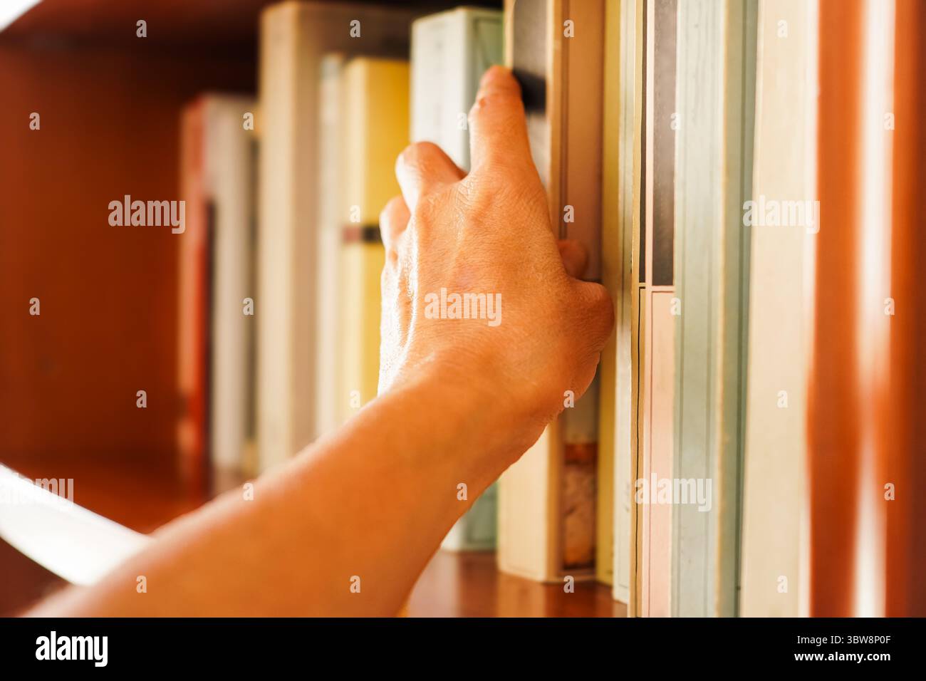 Nahaufnahme einer Hand einer Frau, die versucht, ein Buch aus einem Bücherregal zu holen, Konzepte des Lesens, des Wissens und der Information Stockfoto
