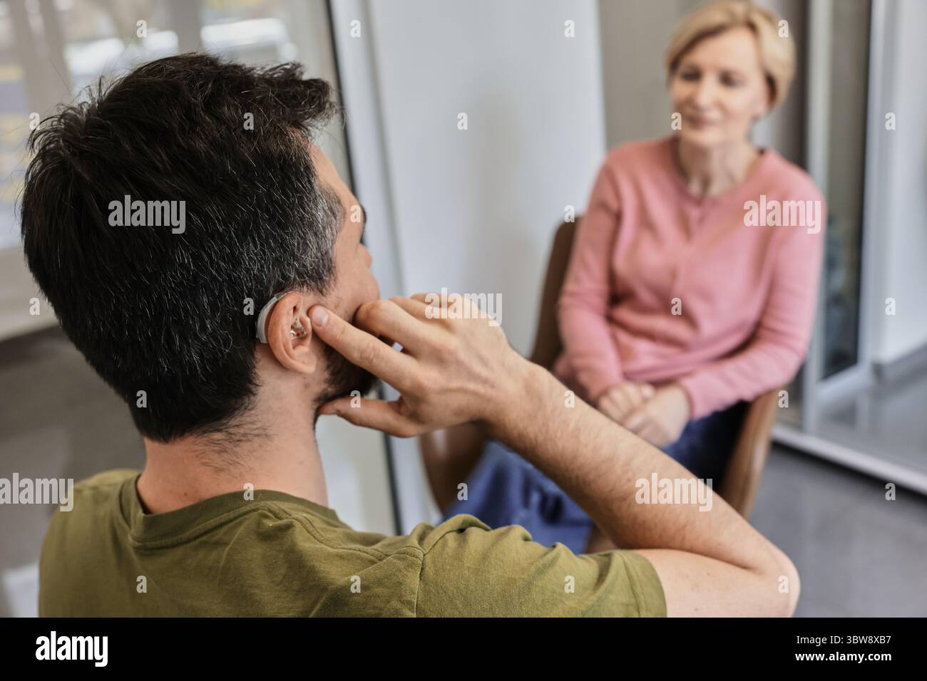 BTE-Hörgerät. Zwei Personen diskutieren aktiv, wobei einer ein Hörgerät verwendet, um ihr Hörerlebnis zu verbessern und sich zu vernetzen Stockfoto