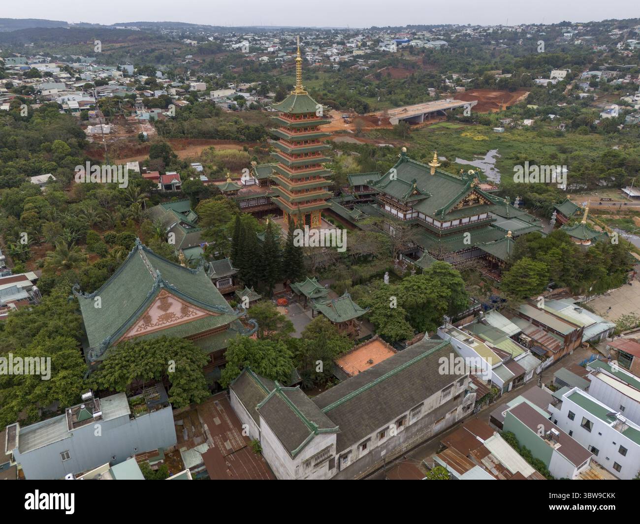 Aus der Vogelperspektive auf die kunstvolle Architektur der Minh Thanh Pagode, mit einer hoch aufragenden Pagode mit einem goldenen Turm inmitten grüner Bäume, Pleiku, Gia Lai, Vietnam Stockfoto