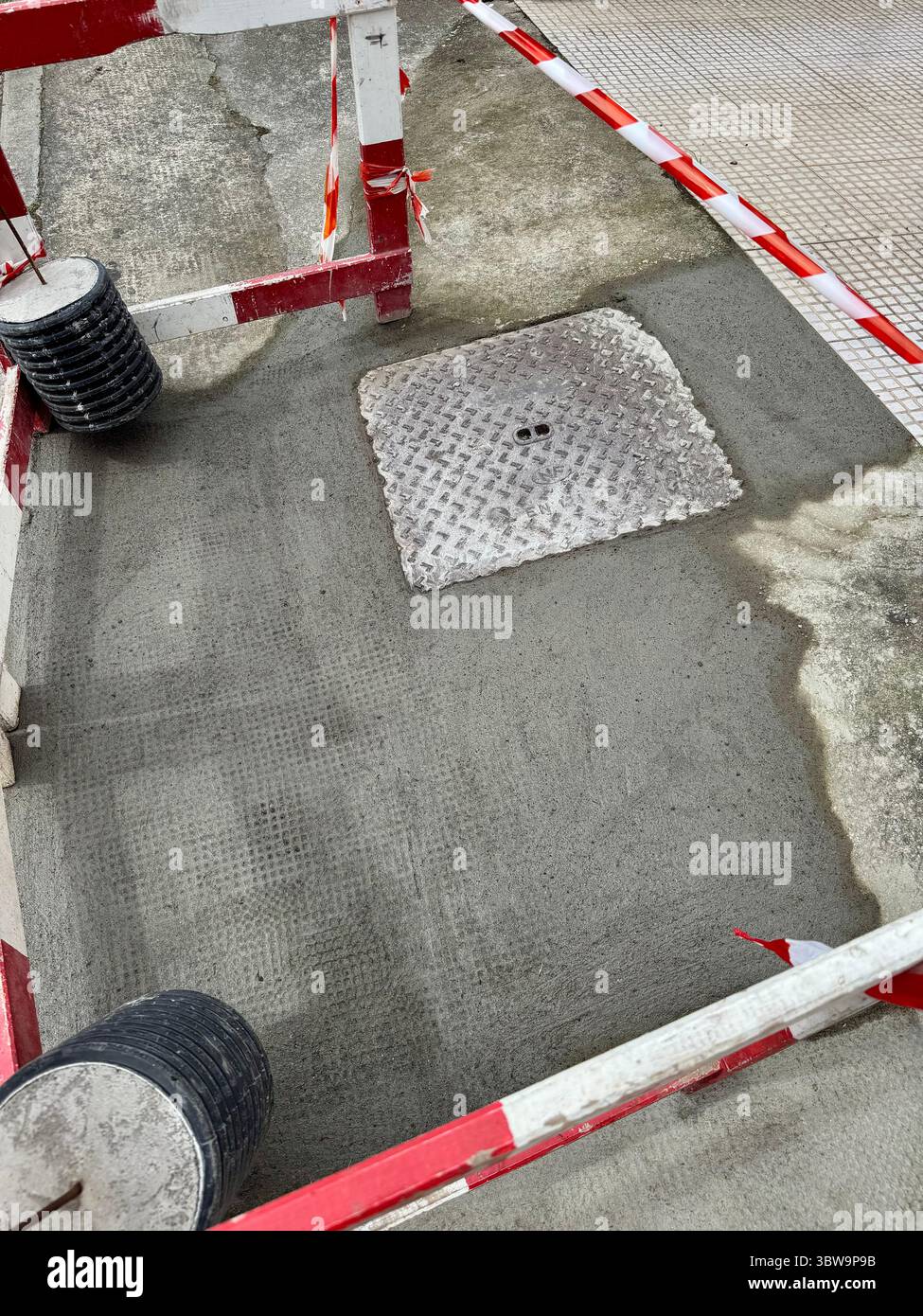 Frisch gegossener Beton um eine Mannlochabdeckung auf einer städtischen Baustelle - Smartphone-aufgenommenes Stockfoto