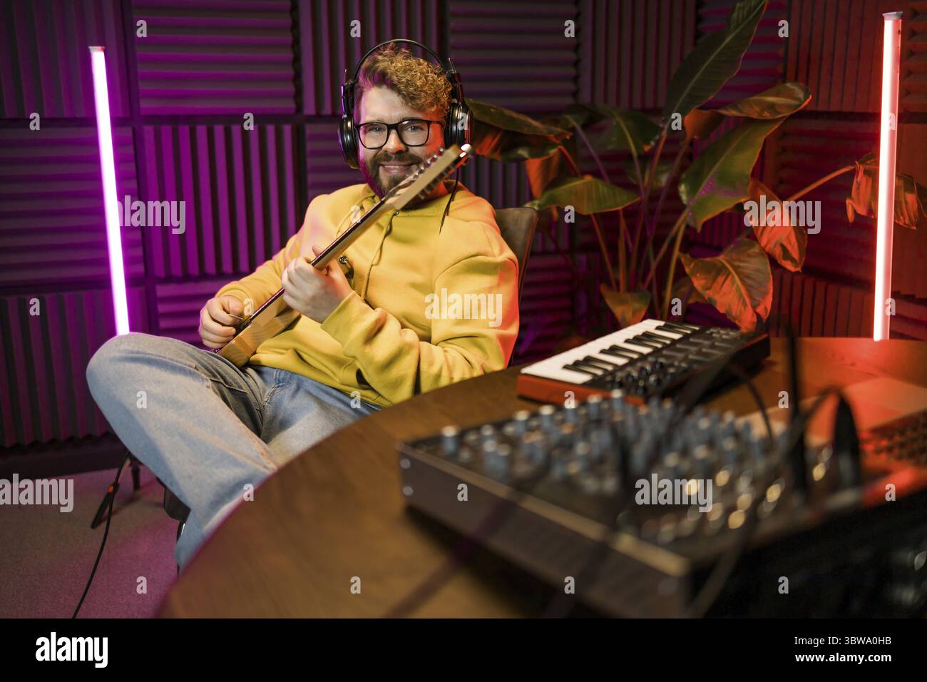 Mann Gesangskünstler singt in einem Tonstudio mit Gitarre. Ein männlicher Sänger singt ein Lied und spielt Gitarre. Soundaufnahme und Musik-Streaming-Konzept Stockfoto