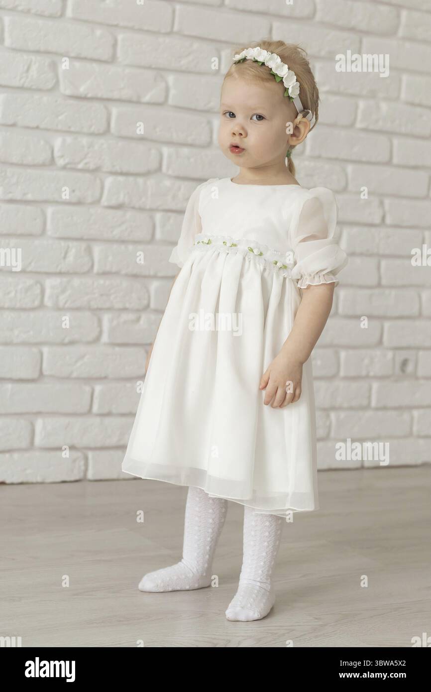 Kleinkind mit Hörgeräten und Cochlea-Implantaten auf weißer Ziegelwand. Taub und Gesundheit und Vielfalt Konzept Stockfoto