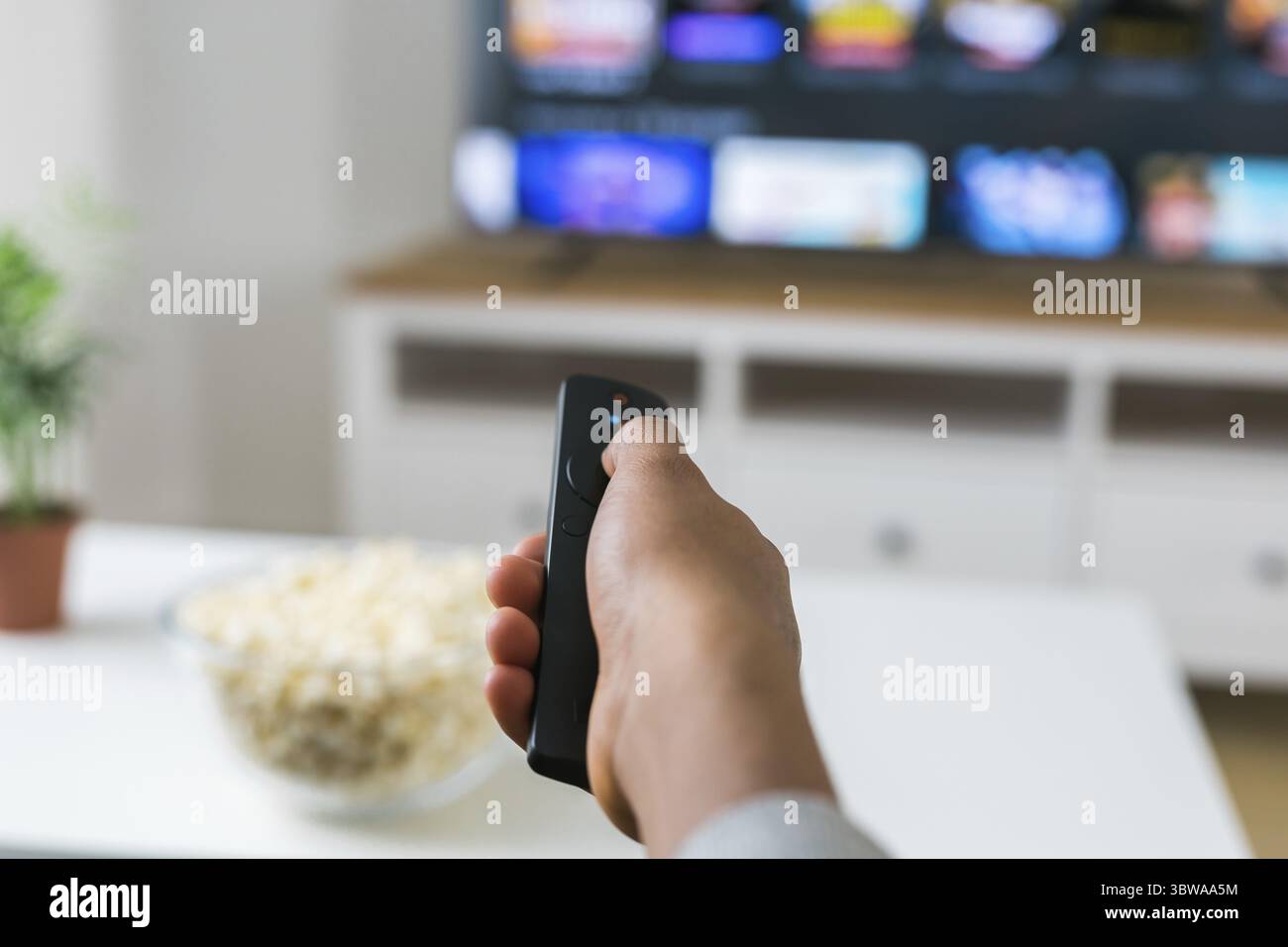 Afroamerikanische Frau sitzt auf einem grauen Sofa und geniesst eine Schuessel Popcorn, waehrend sie einen Film oder einen Online-Streaming-Film Ansie Stockfoto