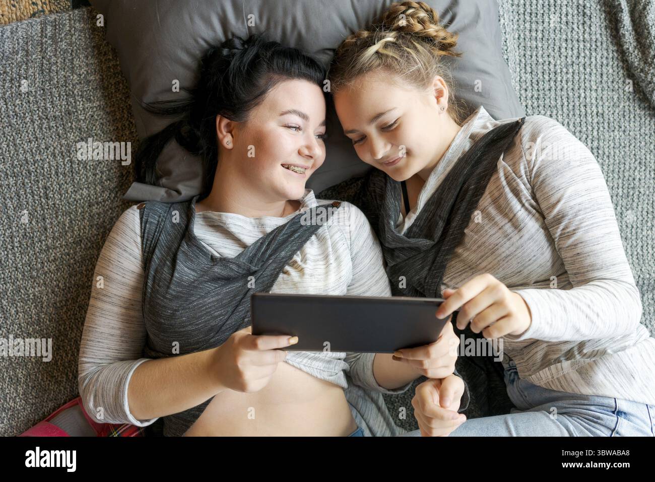 Fröhliche weiße Schwestern liegen auf dem Boden und sehen lustige Videos auf einem digitalen Tablet. Glückliche Beziehung, zu Hause, den freien Tag genießen Stockfoto Fröhliche weiße Schwestern liegen auf dem Boden und sehen lustige Videos auf einem digitalen Tablet. Glückliche Beziehung, zu Hause, den freien Tag genießen Stockfoto