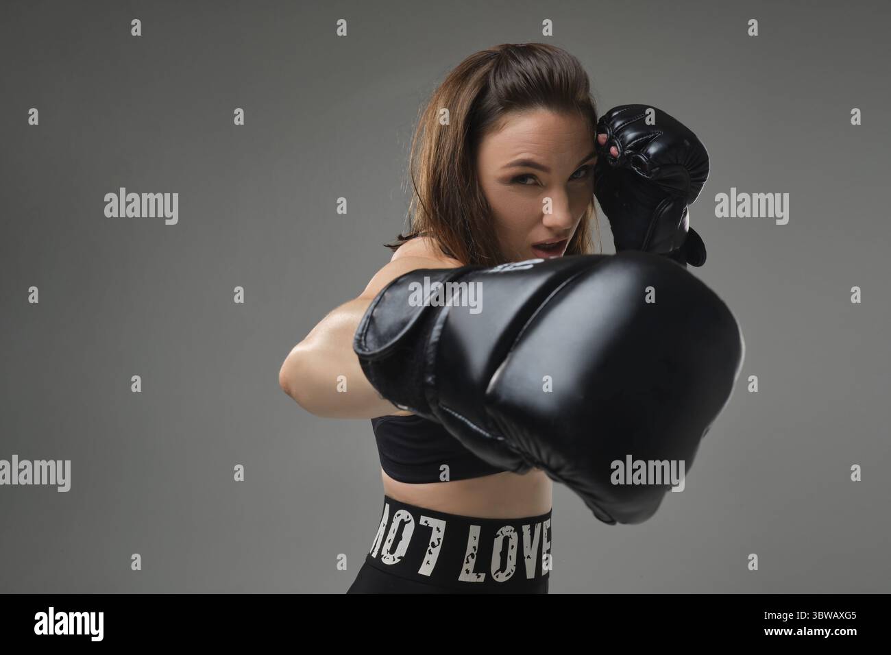 Nahaufnahme eines jungen, wunderschönen Mädchens mit lockeren Haaren, gekleidet in einem Sporttop, Leggings und Boxhandschuhen sieht den Gegner, der K übt Stockfoto