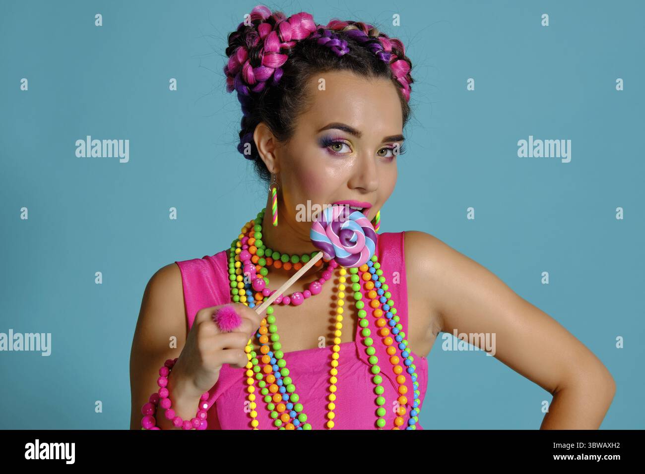 Nahaufnahme von einem attraktiven Maiden mit einem bunten Zöpfe Frisur und Make-up, im Studio vor einem blauen Hintergrund posiert, Essen Stockfoto