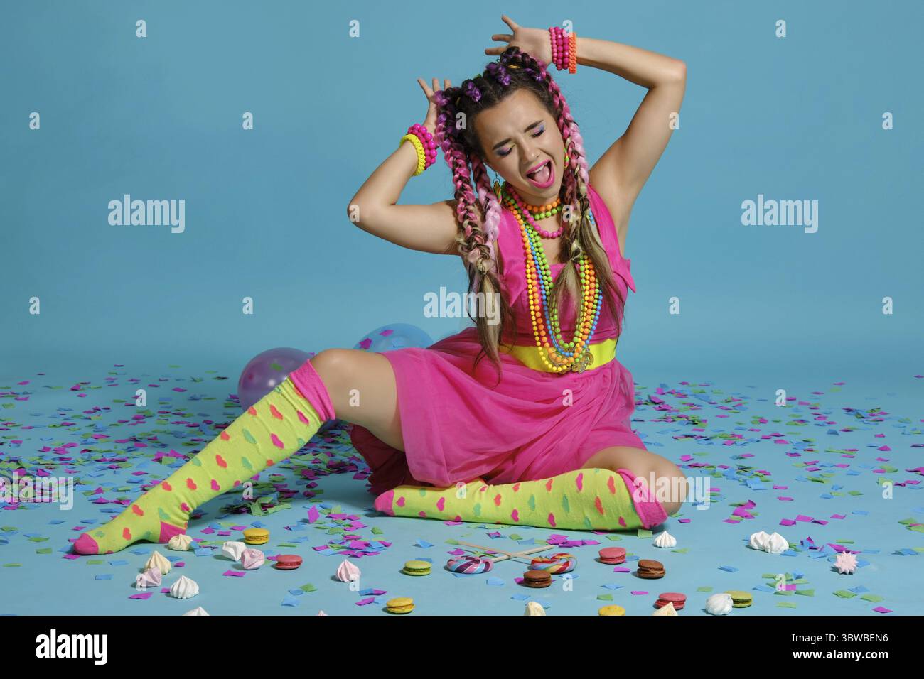 Volle Länge Foto von einer großartigen Frau mit einem bunten Zöpfe Frisur und Make-up. Posiert im Studio mit Luftballons, Macarons, marshmall Stockfoto