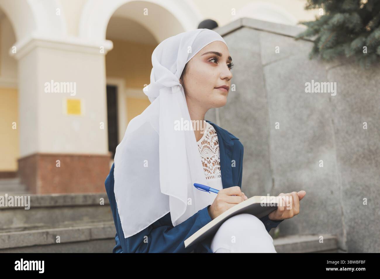 Eine Studentin aus dem Nahen Osten sitzt auf einer Treppe auf dem Universitätsgelände. Bildungs- und Wissenskonzept Stockfoto