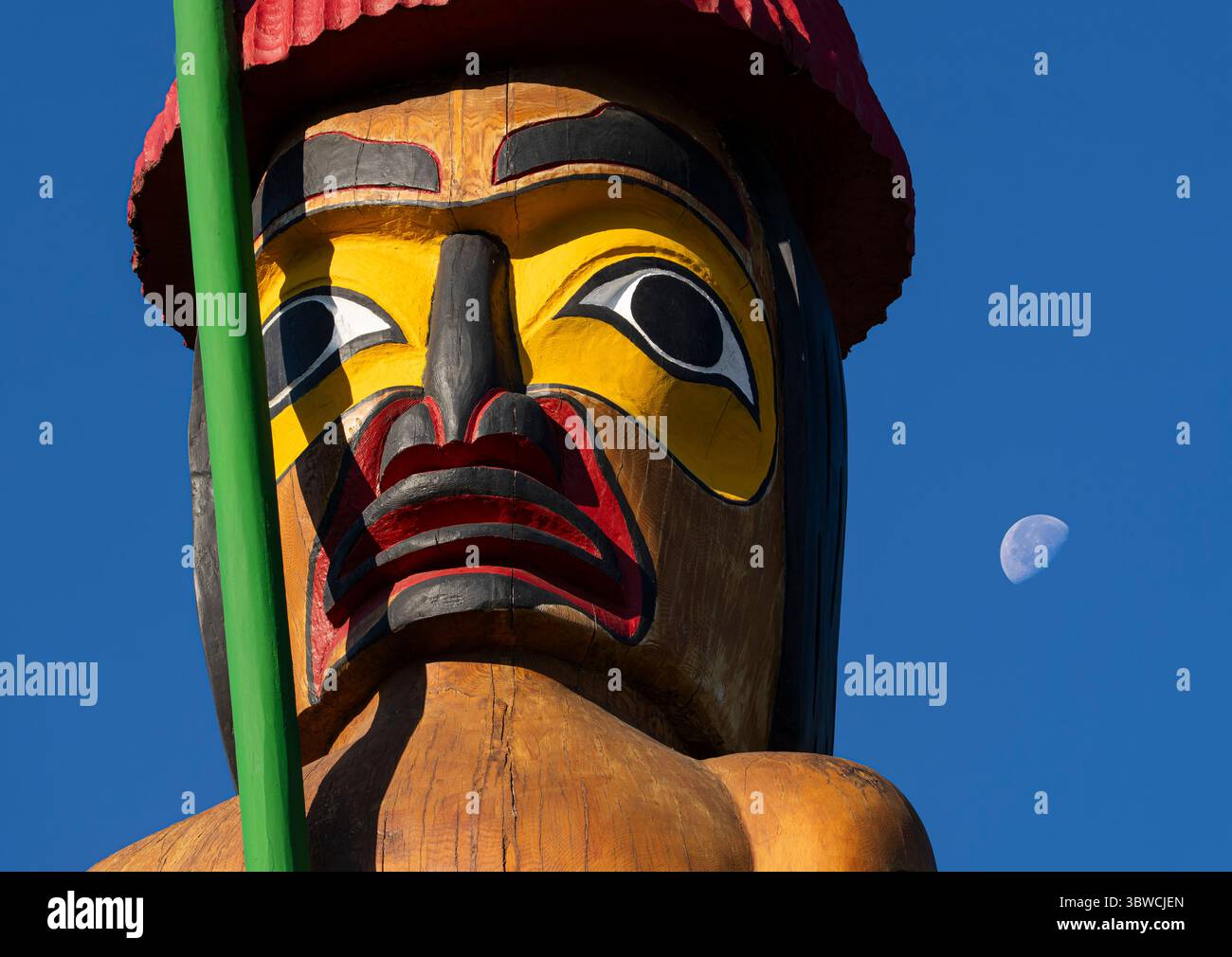 Ein Gesicht auf dem Knowledge Totem Pole mit dem Mond über dem Gelände der Parlamentsgebäude von British Columbia in Victoria. Stockfoto