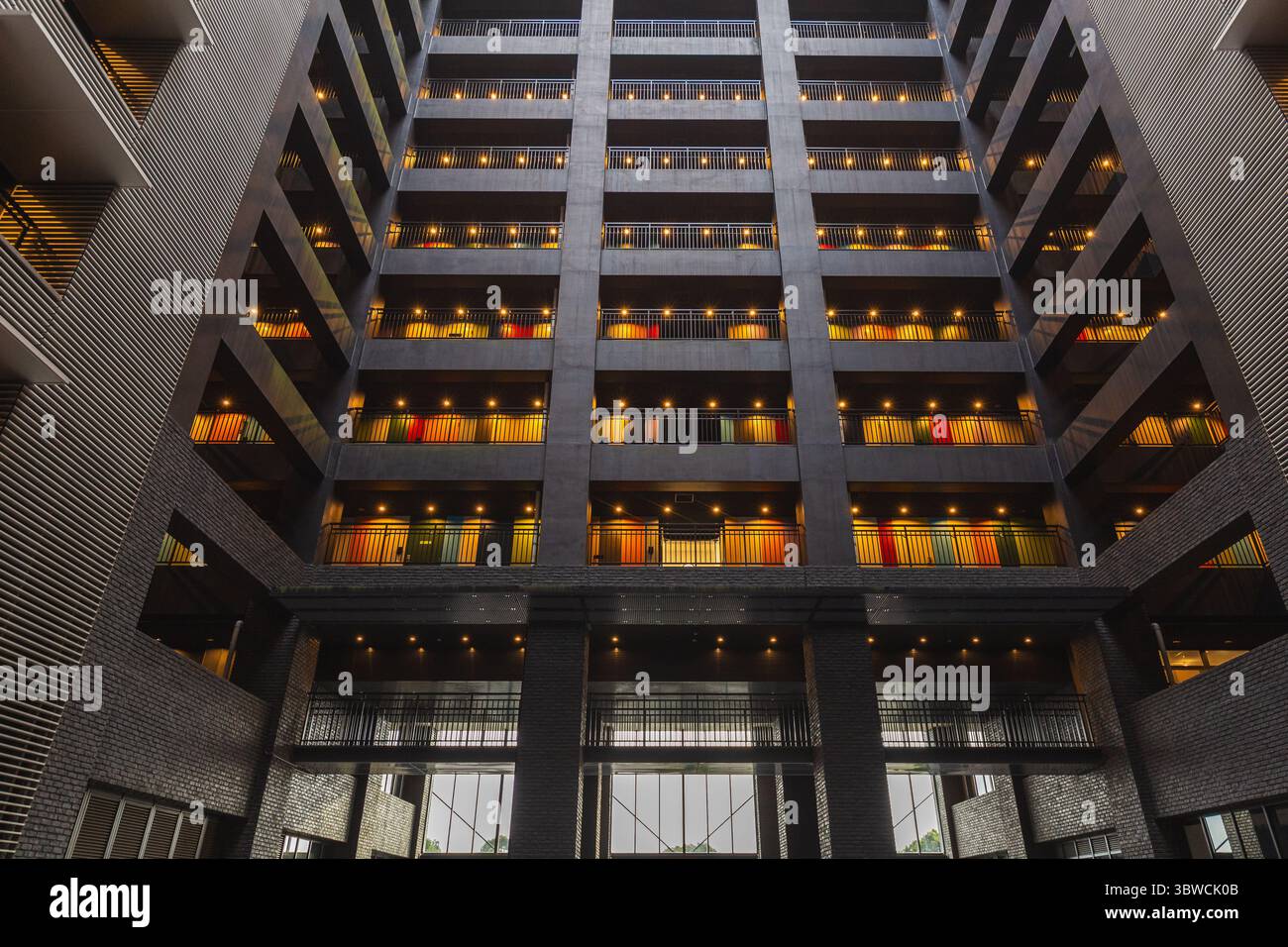 Modernes Innenleben mit zahlreichen Balkonen mit farbenfrohen Türen, die von warmer Beleuchtung beleuchtet werden. Das architektonische Design betont geometrische Elemente Stockfoto
