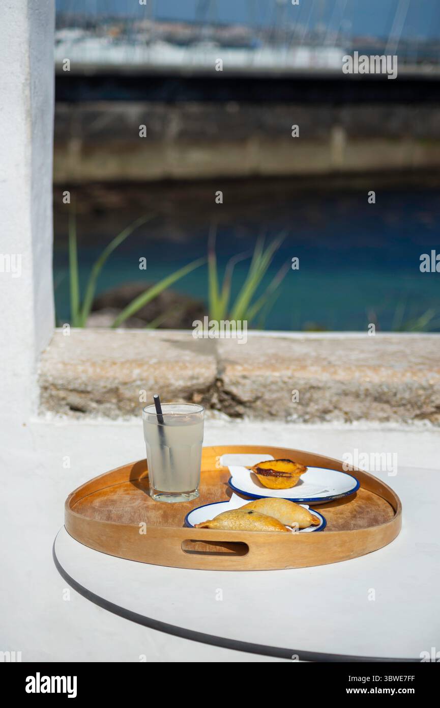 Cascais, Portugal: Erfrischende, hausgemachte Limonade und köstliches Pastell de Nata auf einem hellen Holztablett vor einer ruhigen Küstenkulisse Stockfoto