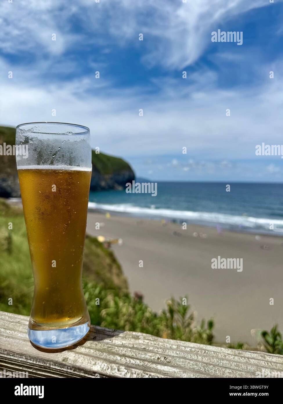 Ein Glas kaltes Bier mit Panoramablick auf das Meer am Strand Santa Bárbara, Insel São Miguel, Azoren, Portugal. - Smartphone-aufgenommenes Stockfoto