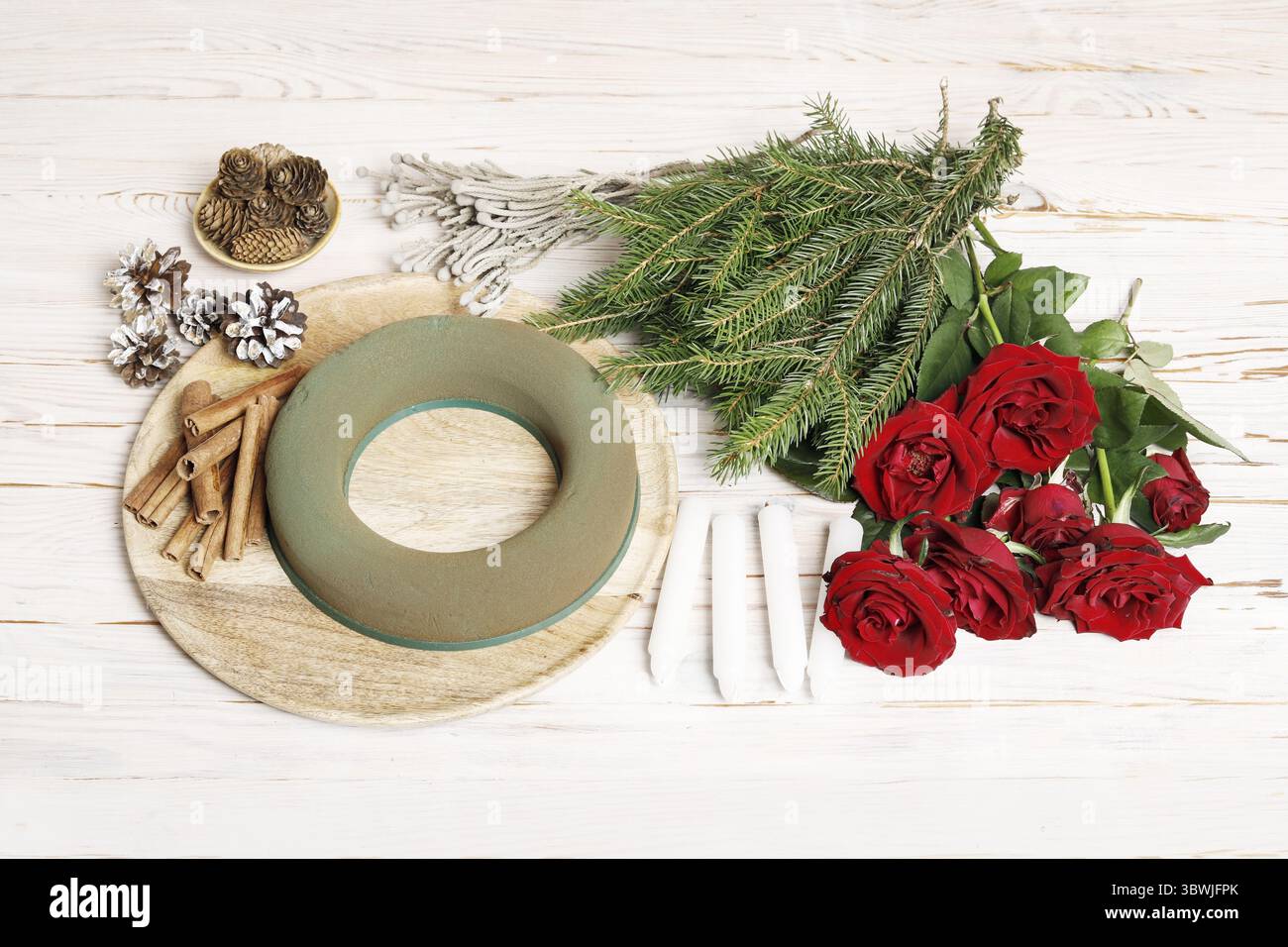 Florist bei der Arbeit: Wie man einen traditionellen Adventskranz für den Tisch aus Rosenblüten, Tannenzweigen und zusätzlichen Elementen bastelt. Stockfoto